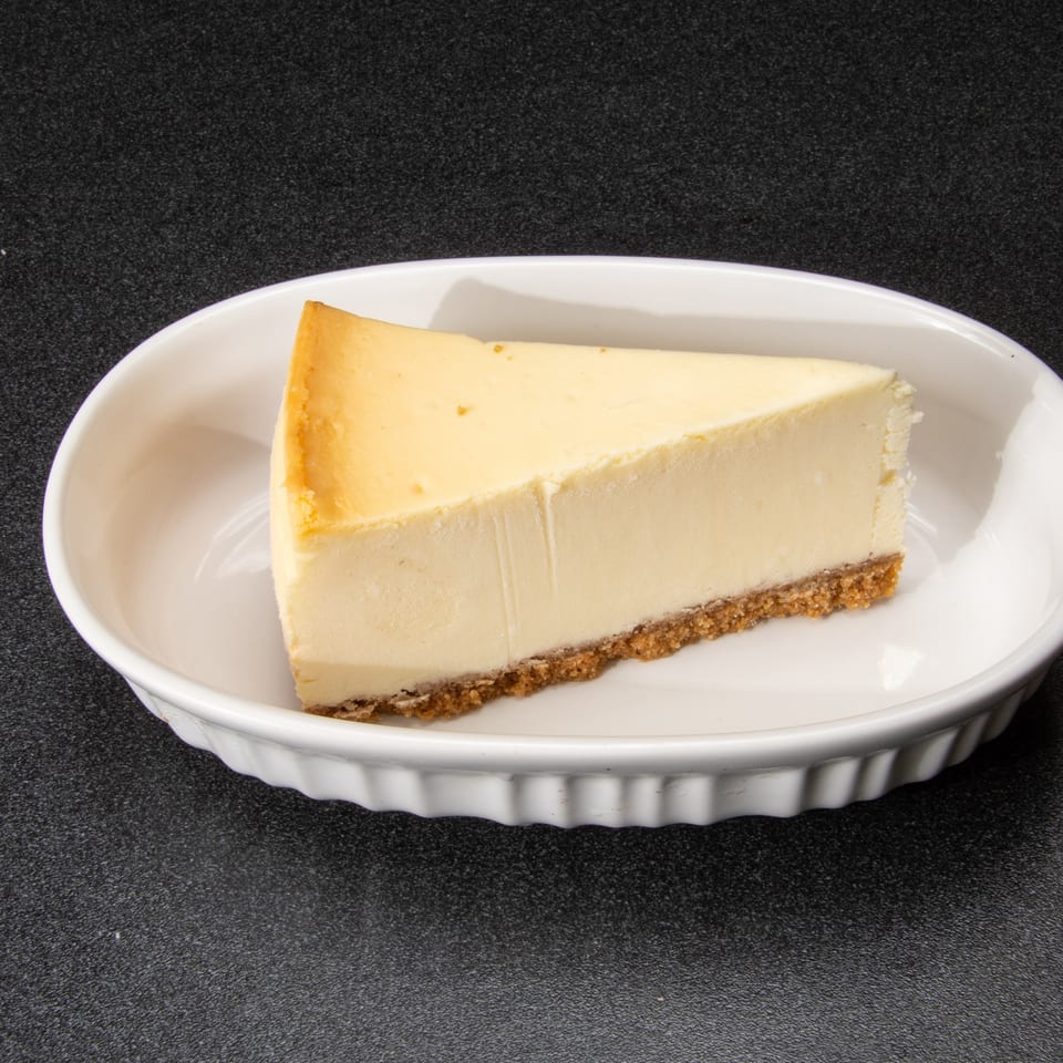 Slice of plain cheesecake with a golden crust served on a white oval plate.