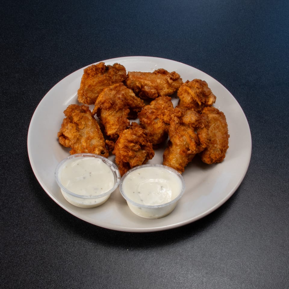 Plate of crispy fried chicken pieces served with two cups of creamy dipping sauce on a dark tabletop.