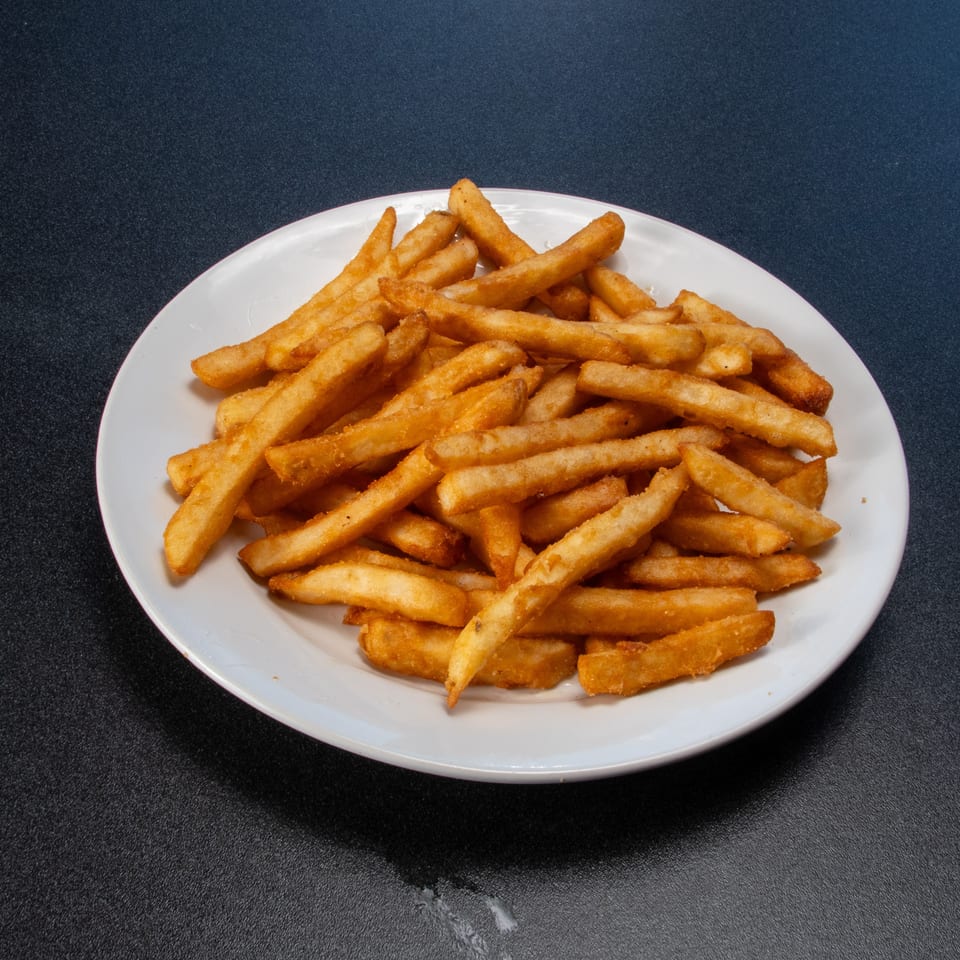 A white plate piled with golden French fries sits on a dark tabletop.