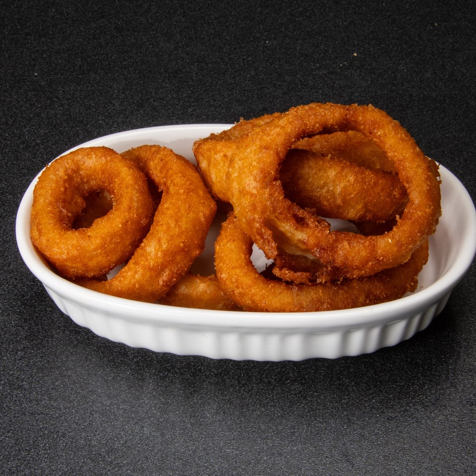 Crispy golden-brown onion rings piled in a white dish on a black textured surface.