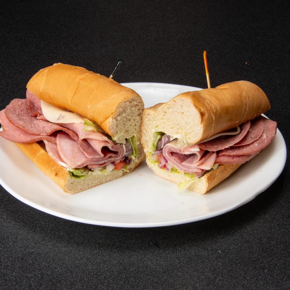 Two deli meat and cheese sandwiches with lettuce and vegetables on a white plate, secured with toothpicks.